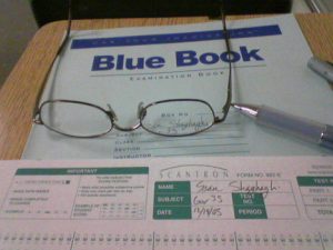 Photo of exam Blue Book, test form, glasses, and pen